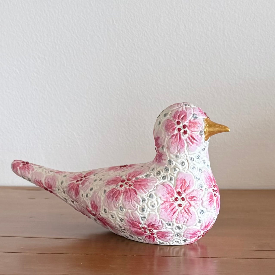 Decorative ceramic bird figurine with floral pattern on a wooden surface