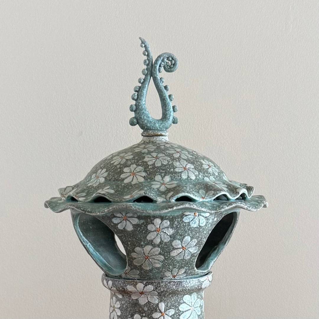 Top of decorative ceramic lantern with Daisy pattern & finial on a plain background