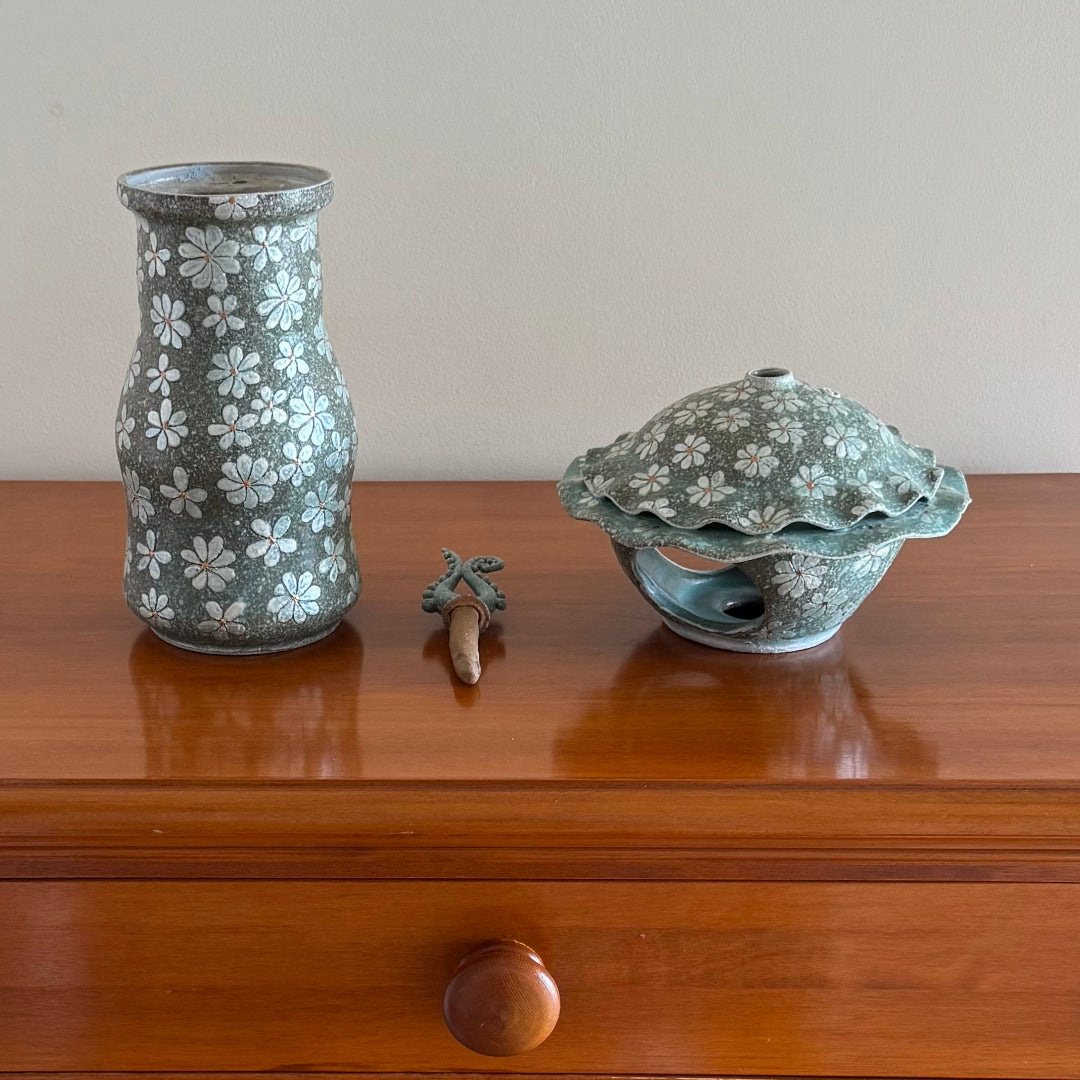 3 Pieces that make up a decorative ceramic Lantern including the base, lantern , and finial on a wooden surface.