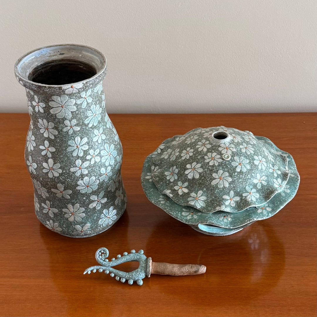 3 Pieces that make up a decorative ceramic Lantern including the base, lantern , and finial on a wooden surface.