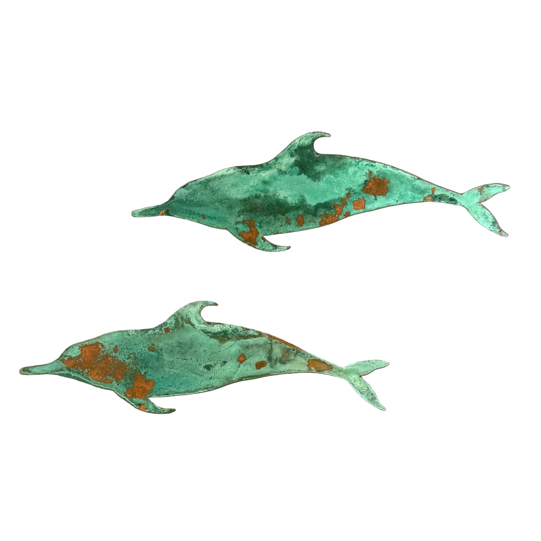 Two copper green patina'd dolphins on a white background