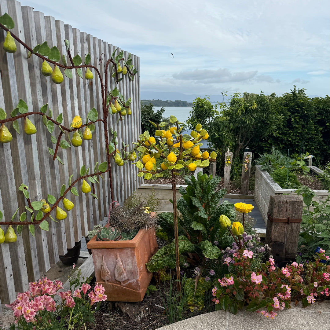 Ceramic lemon tree in garden scene with succulents, and flowers.