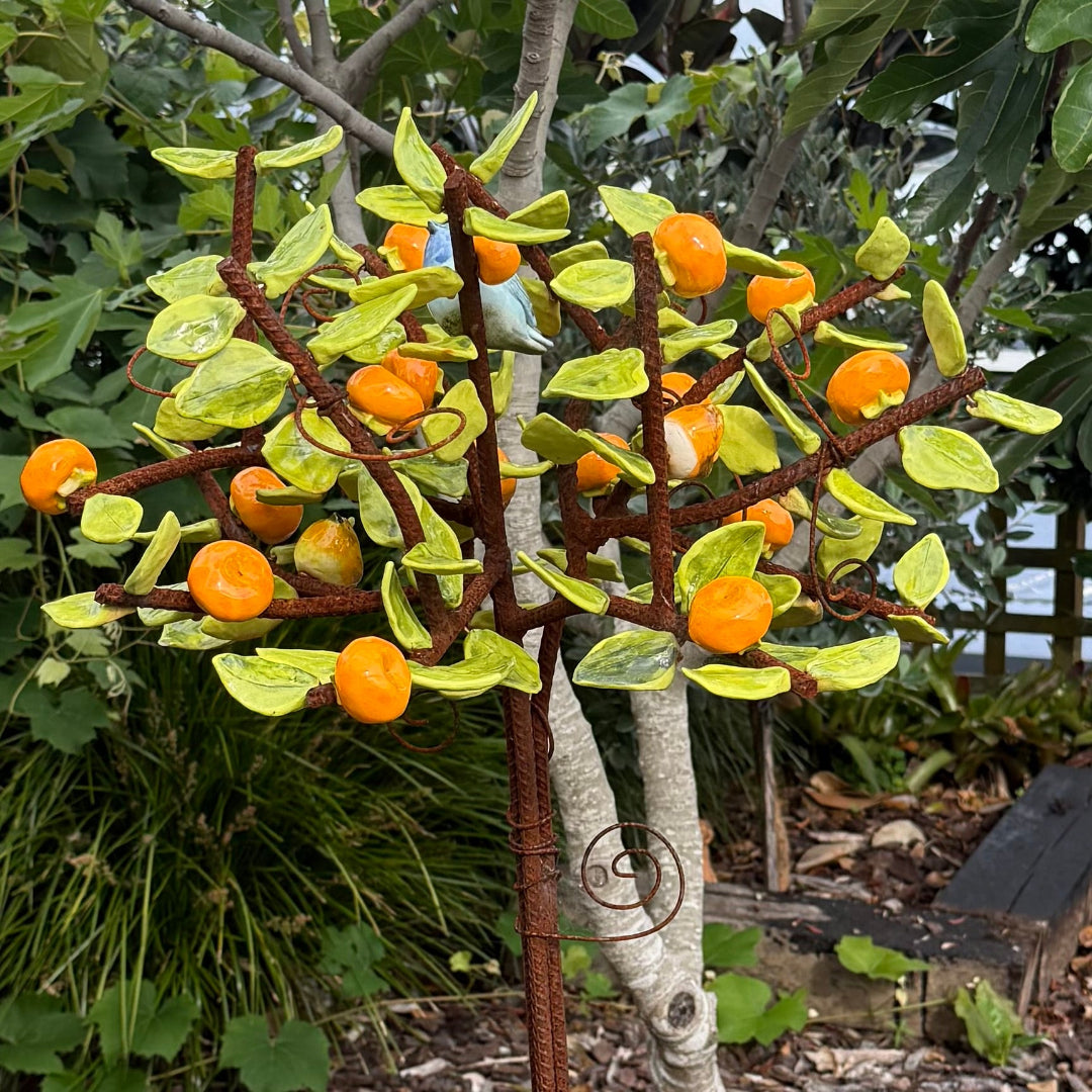 Decorative ceramic tree with orange mandarins and green leaves with a small bird in a garden setting