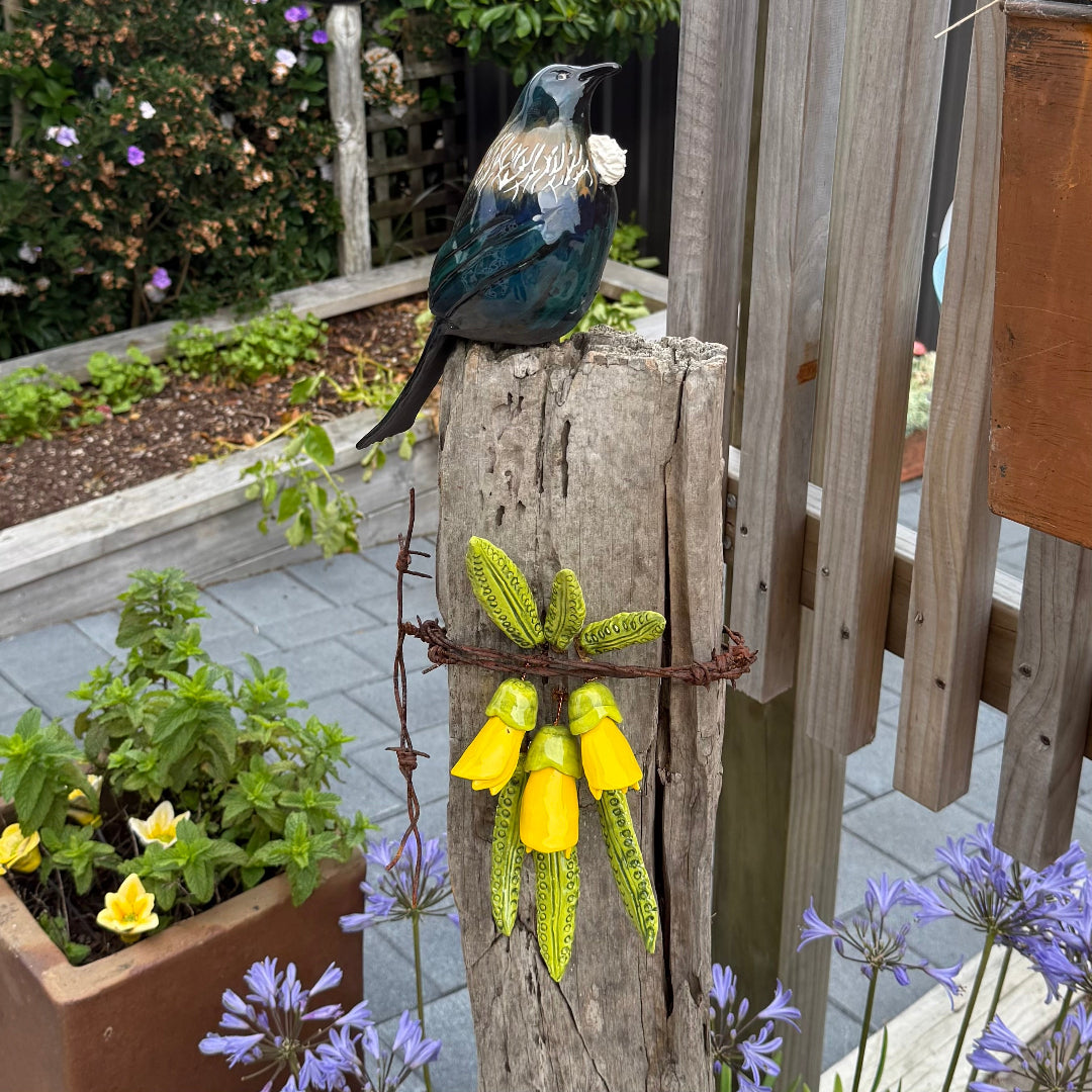 Ceramic Tui bird sculpture on a wooden post with a garden background