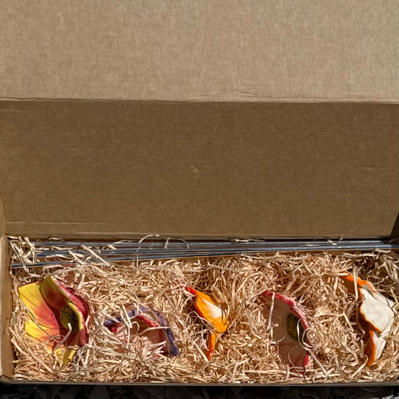 Set of colorful ceramic wildflowers with stainless steel stems on straw in a cardboard box