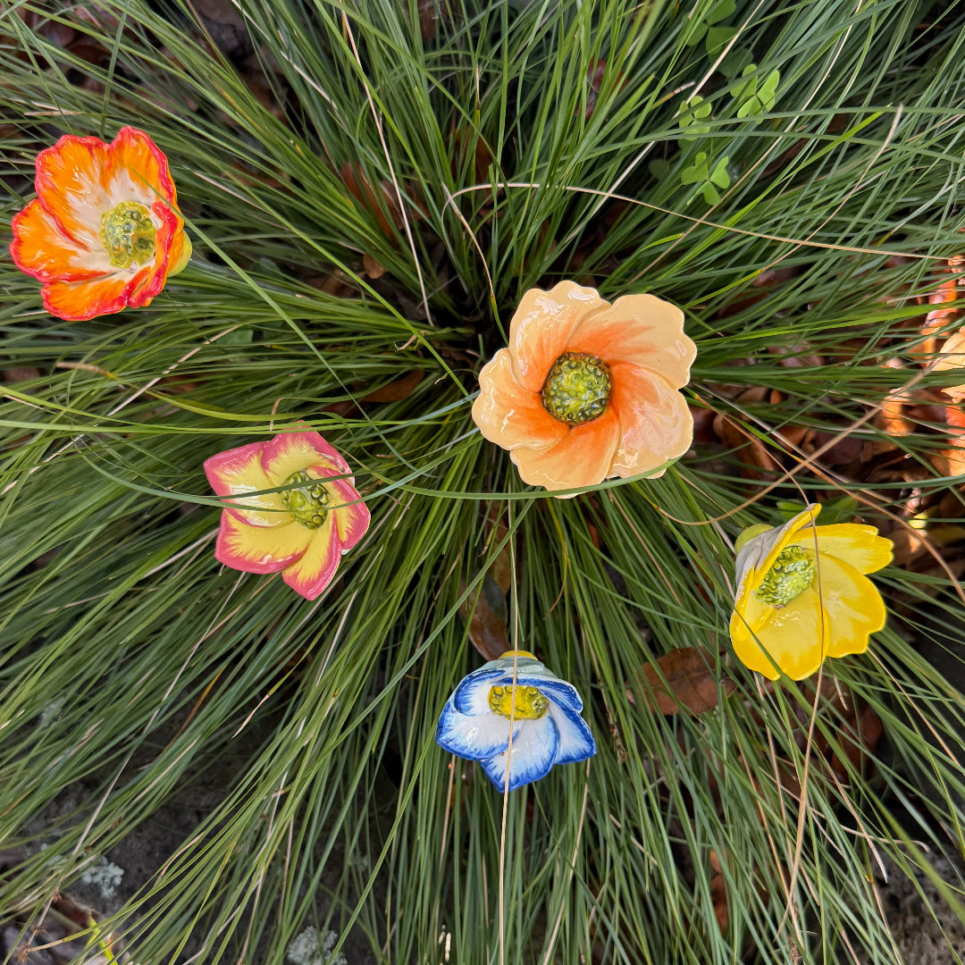 Decorative ceramic flowers on steel rods in various colours on a green plant background