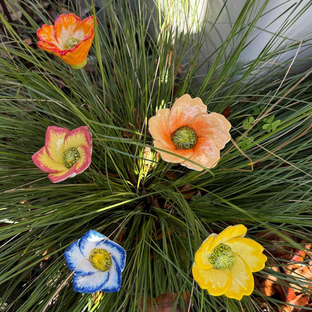 Decorative ceramic flowers on steel rods in various colours on a green plant background