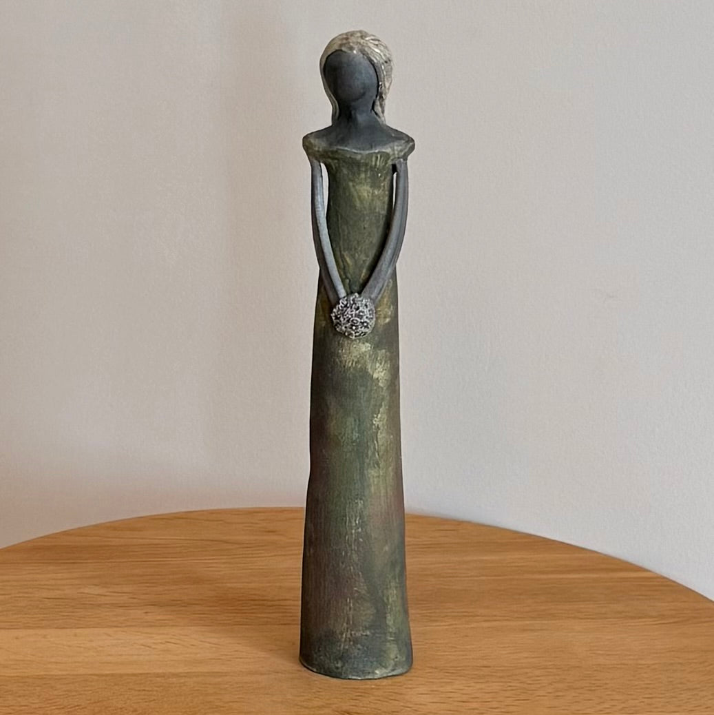 Ceramic statue of a woman holding a posy on a wooden surface with a beige background