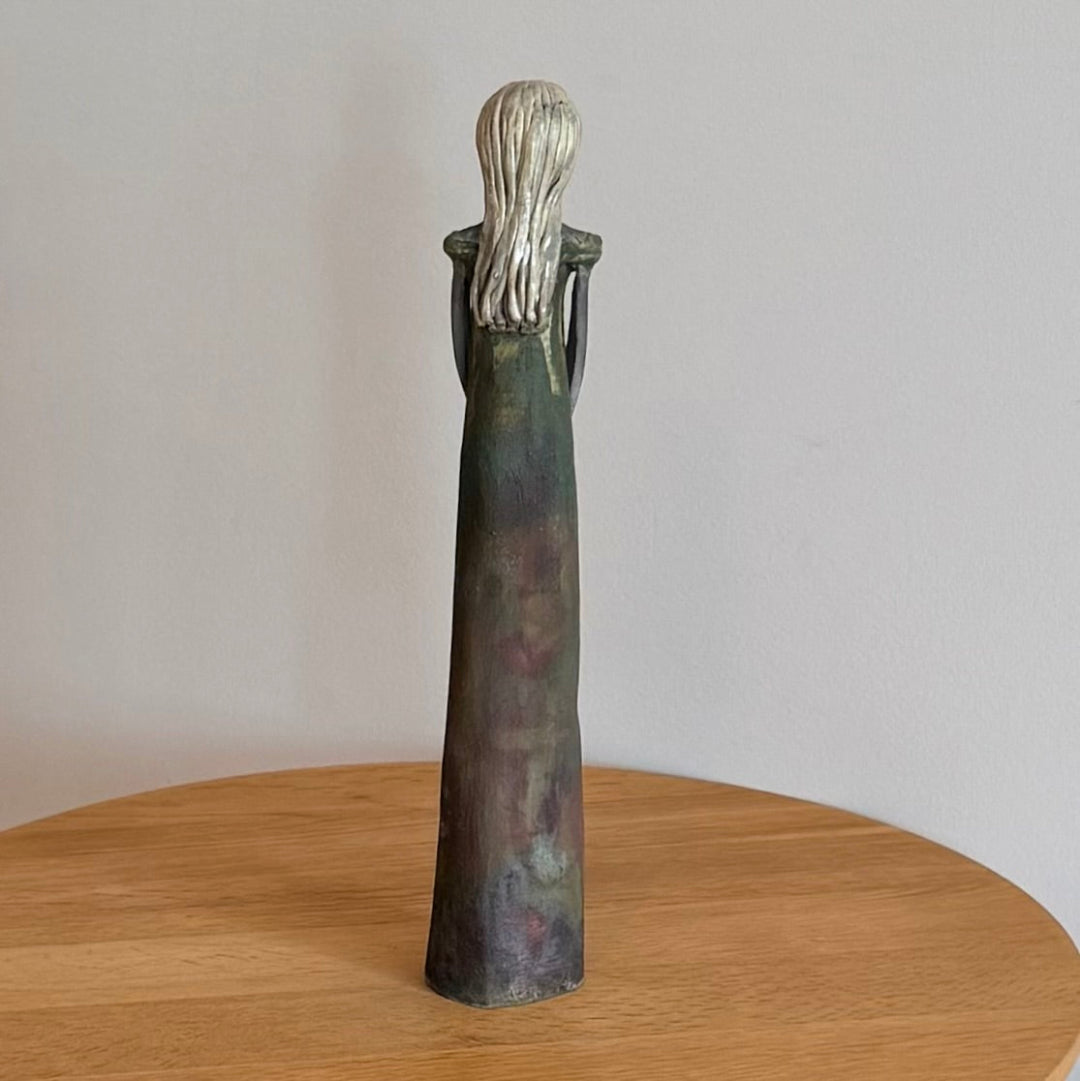 Back view of a ceramic sculpture of a standing figure on a wooden surface with a plain background