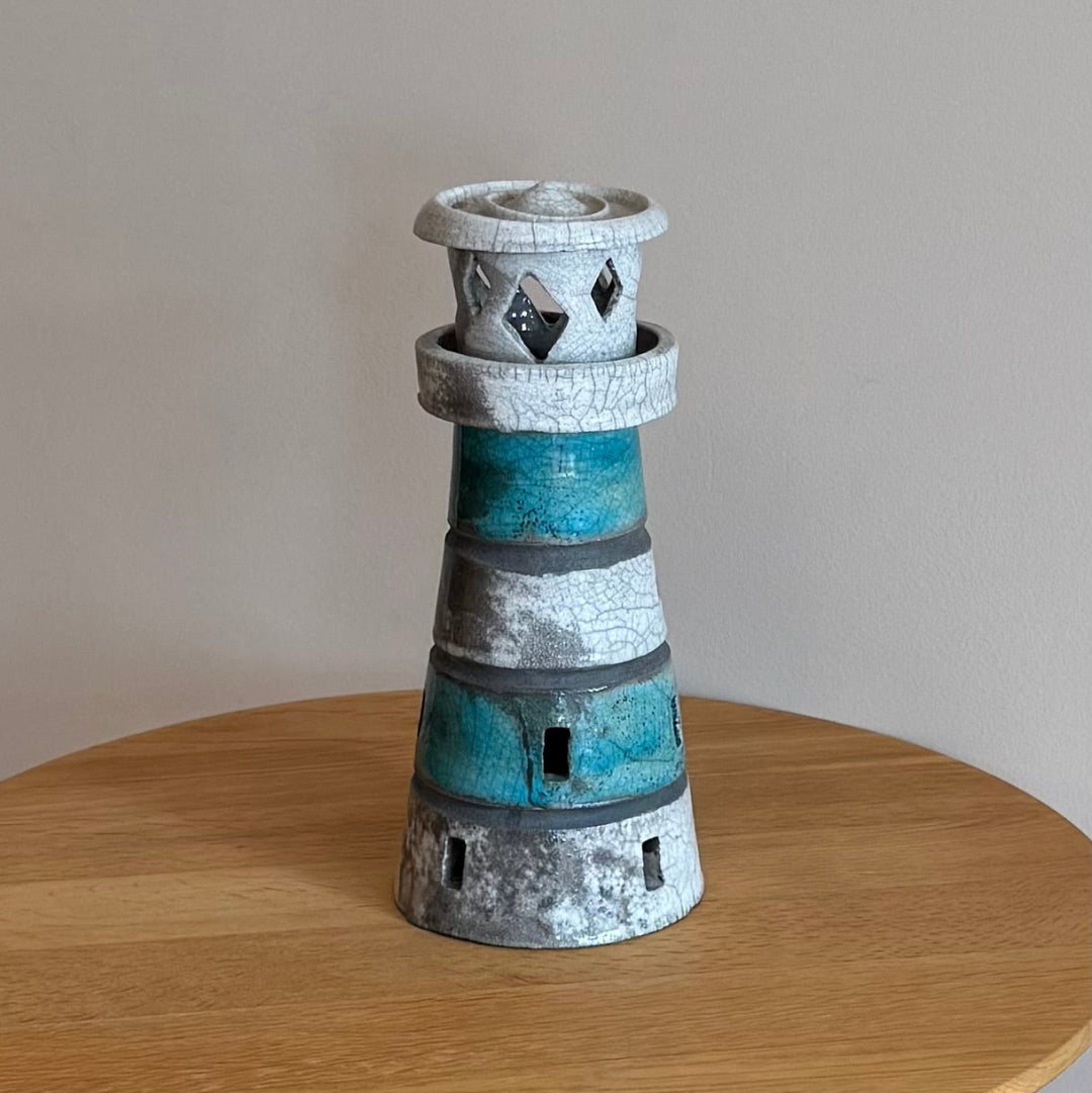 Ceramic lighthouse tealight holder sculpture on a wooden surface with a plain background