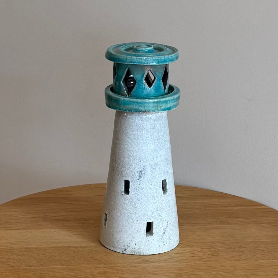 Ceramic lighthouse tealight holder sculpture on a wooden surface with a plain backgroundsurface.