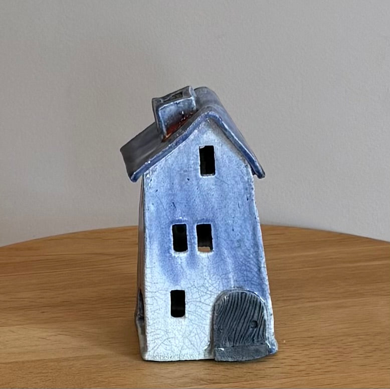 Ceramic house-shaped telight holder with a blue glaze on a wooden surface.