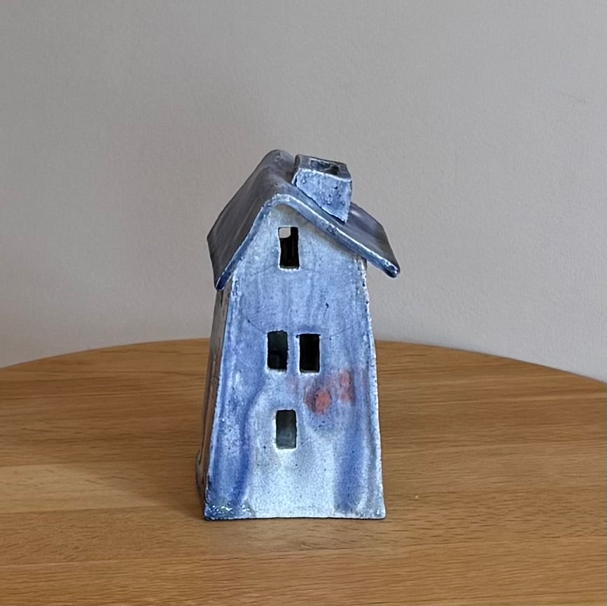 Ceramic house-shaped telight holder with a blue glaze on a wooden surface.