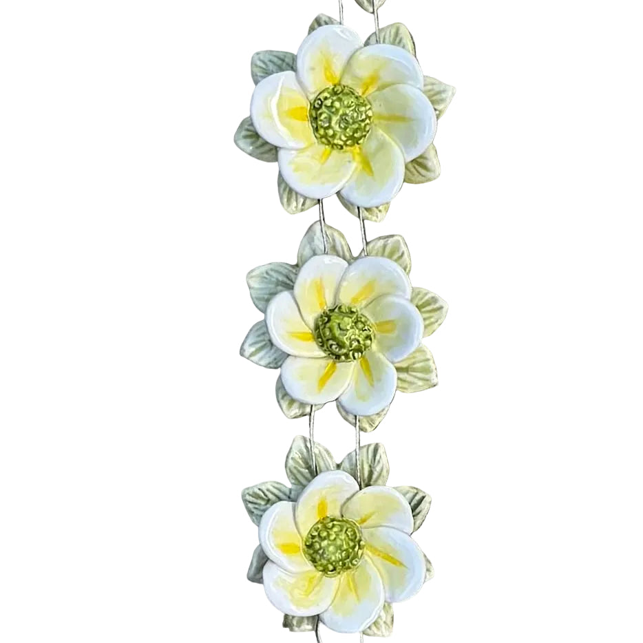 Decorative floral wall hanging with yellow, white and green ceramic flowers on a white surface