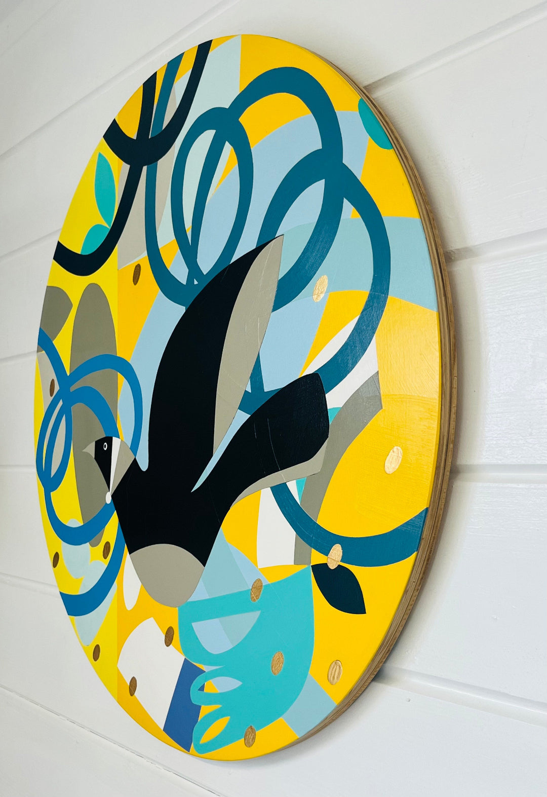 Side view of a round painting of a Tui with abstract design on a white wall