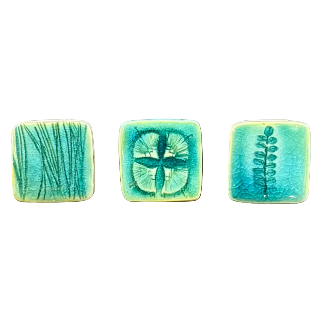 Three square ceramic tiles with green and blue plant patterns on a white surface