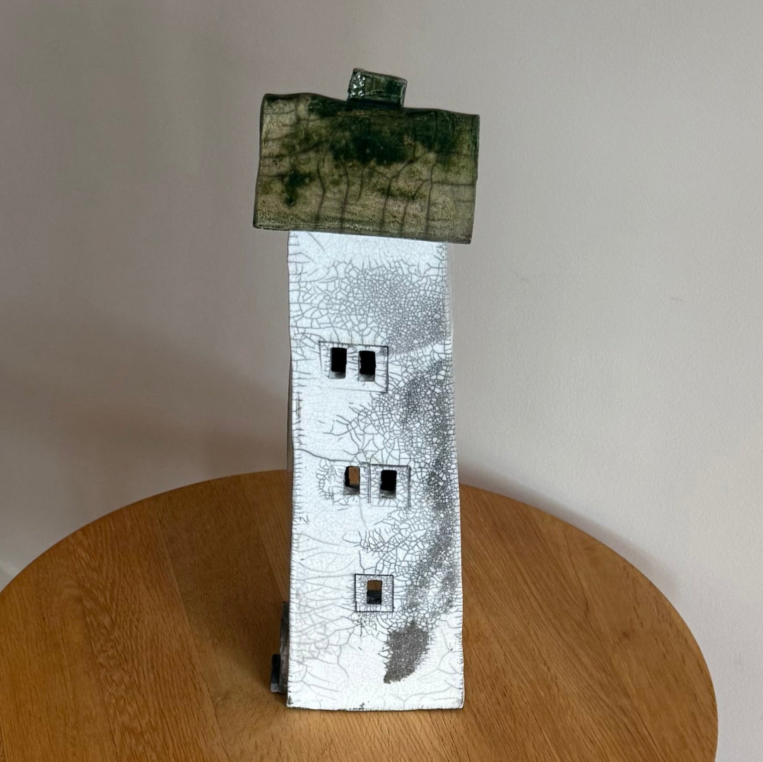 Ceramic tall house with a green roof on a wooden surface side view