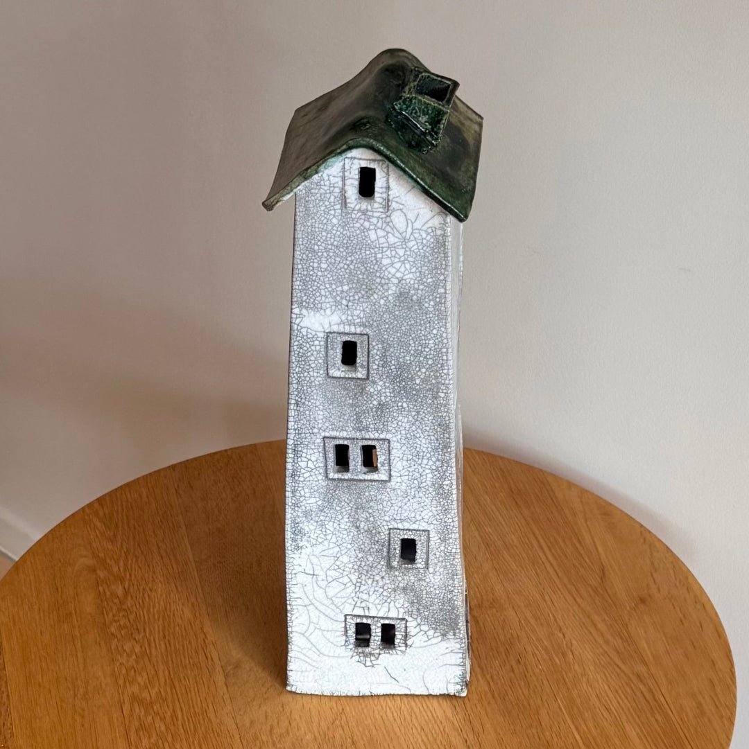 Ceramic tall house with a green roof on a wooden surface side view