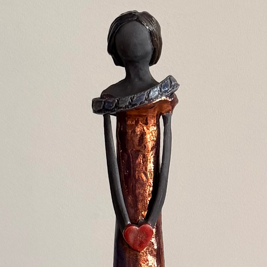 Close up half view of a ceramic figurine holding a heart on a plain background