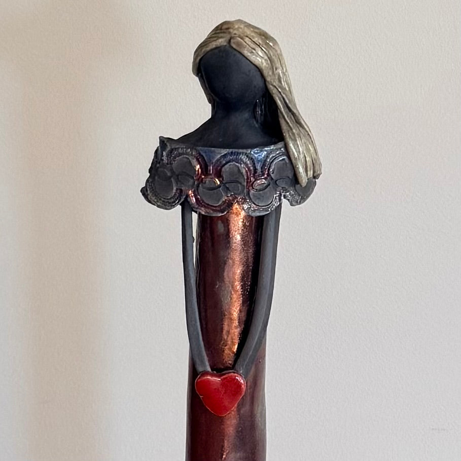 Close up view of a ceramic figurine of a woman holding a heart on a plain background