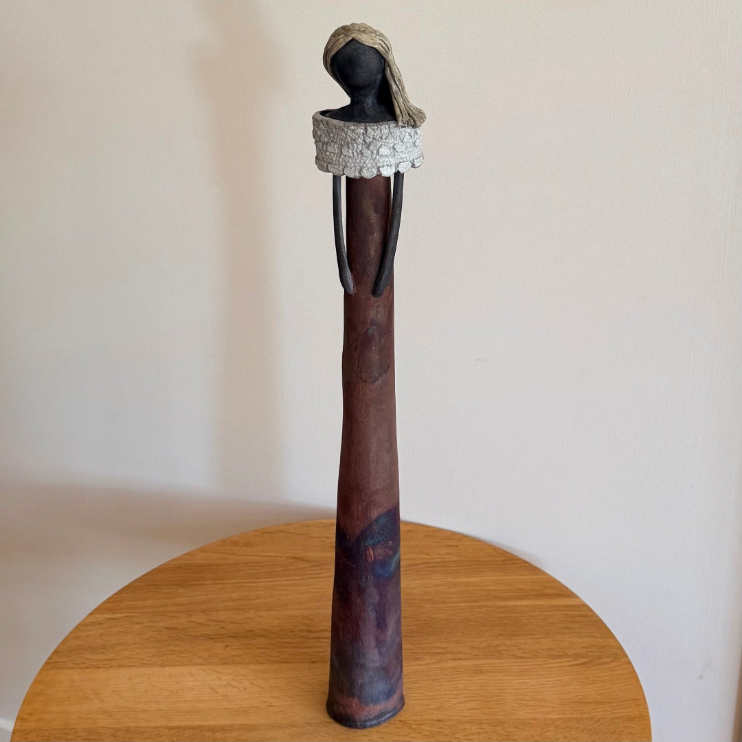 Ceramic figure with matt finish on a wooden table against a plain background
