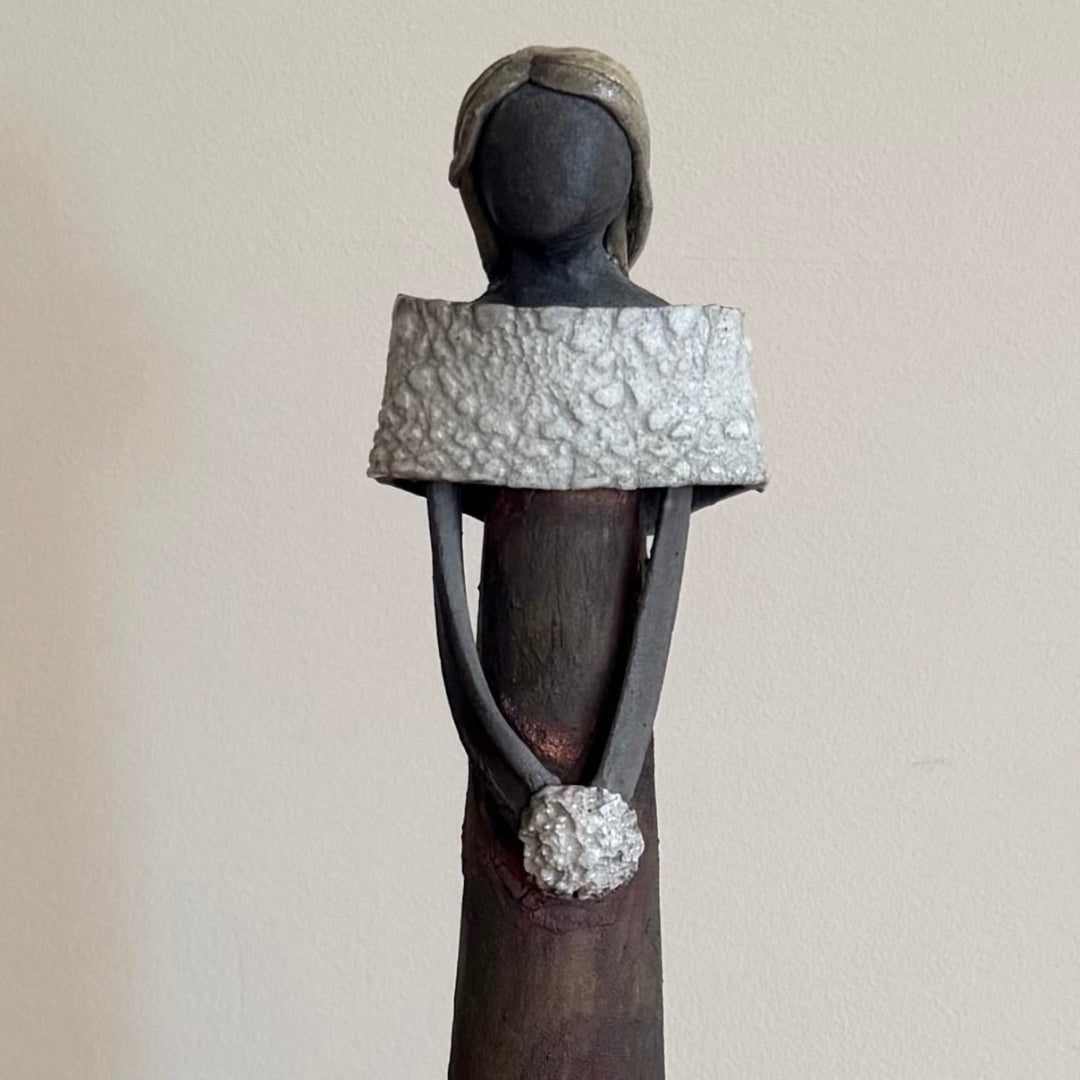 Close up view of a ceramic lady holding a white posy against a plain background