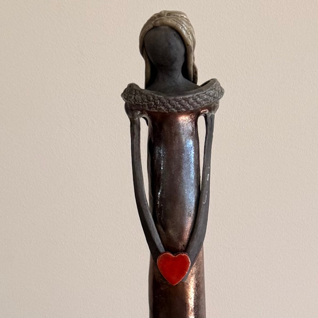 Close up view of a ceramic figurine with a red heart on a plain background