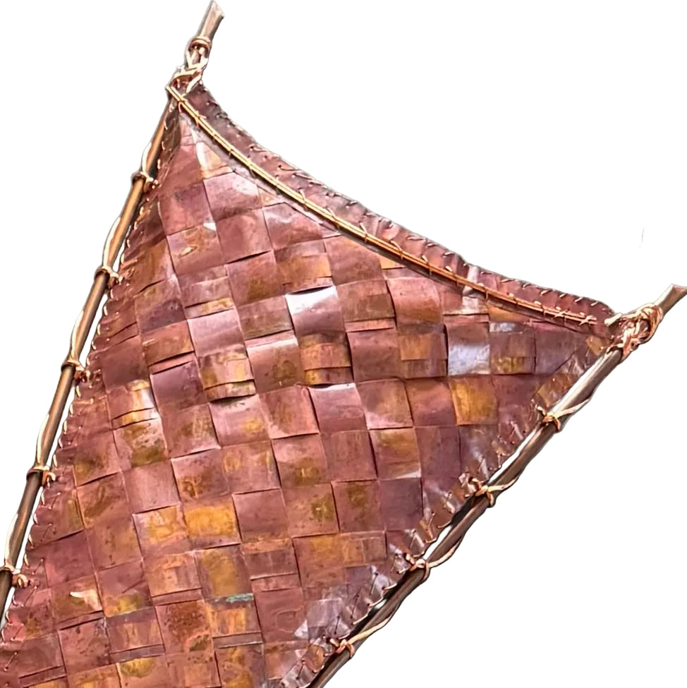 Close up of the top section of a decorative sail-shaped woven copper wall scupture on a white background