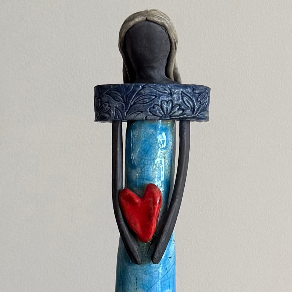 Close up of ceramic figurine holding a red heart on a gray background