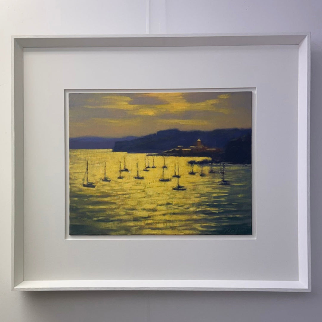 Framed artwork of a sunset over a body of water with sailboats and a mountain.