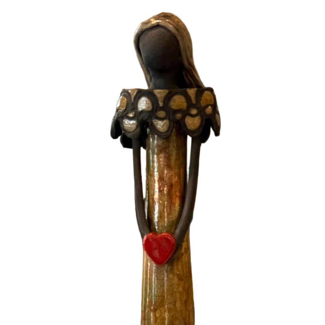 Close up view of a tall, decorative ceramic lady with a yellow glaze holding a red heart on a white background