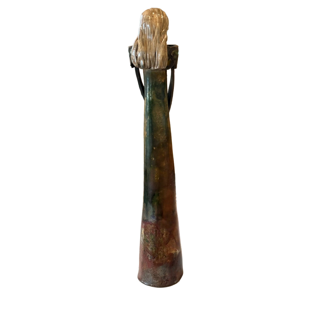 A tall, narrow sculptural figurine with a textured metallic top and a dark, earthy body, displayed on a white backgound.
