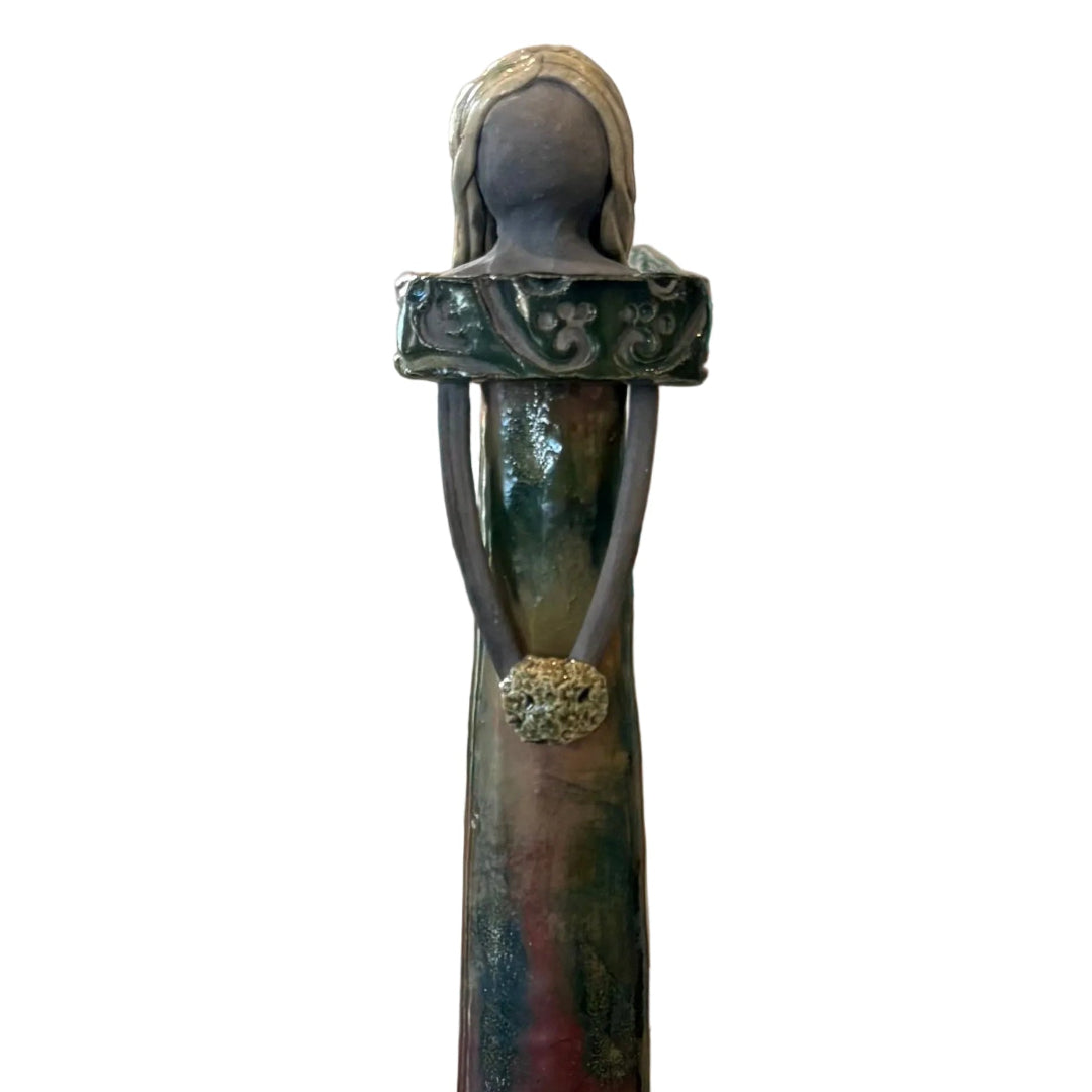 A close up view of a tall, slender ceramic sculpture of a woman with a white background.