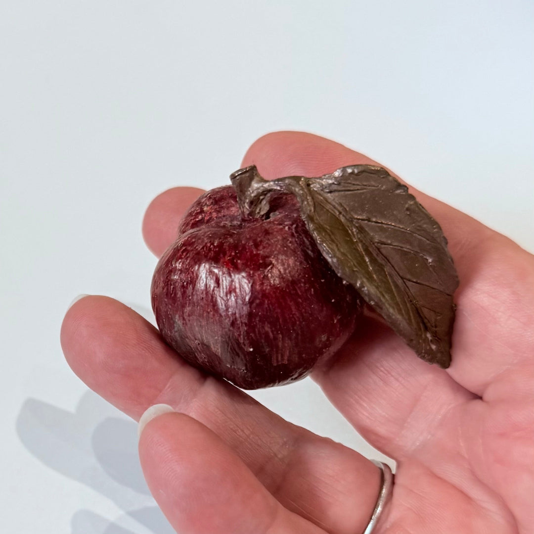 Hand holding a painted bronze miniature peach with a leaf on a white background