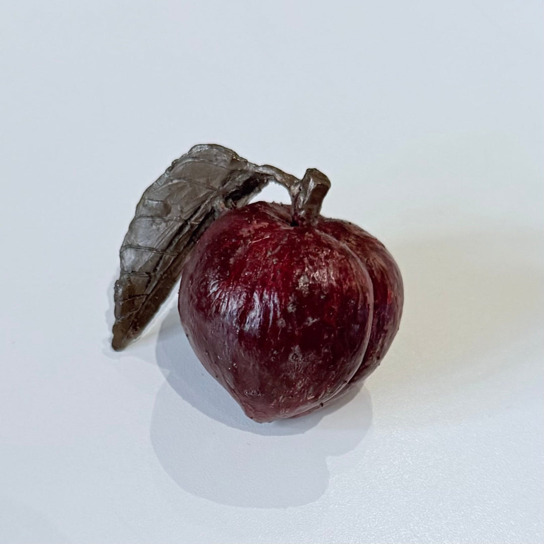 Painted bronze miniature peach with a leaf on a white background