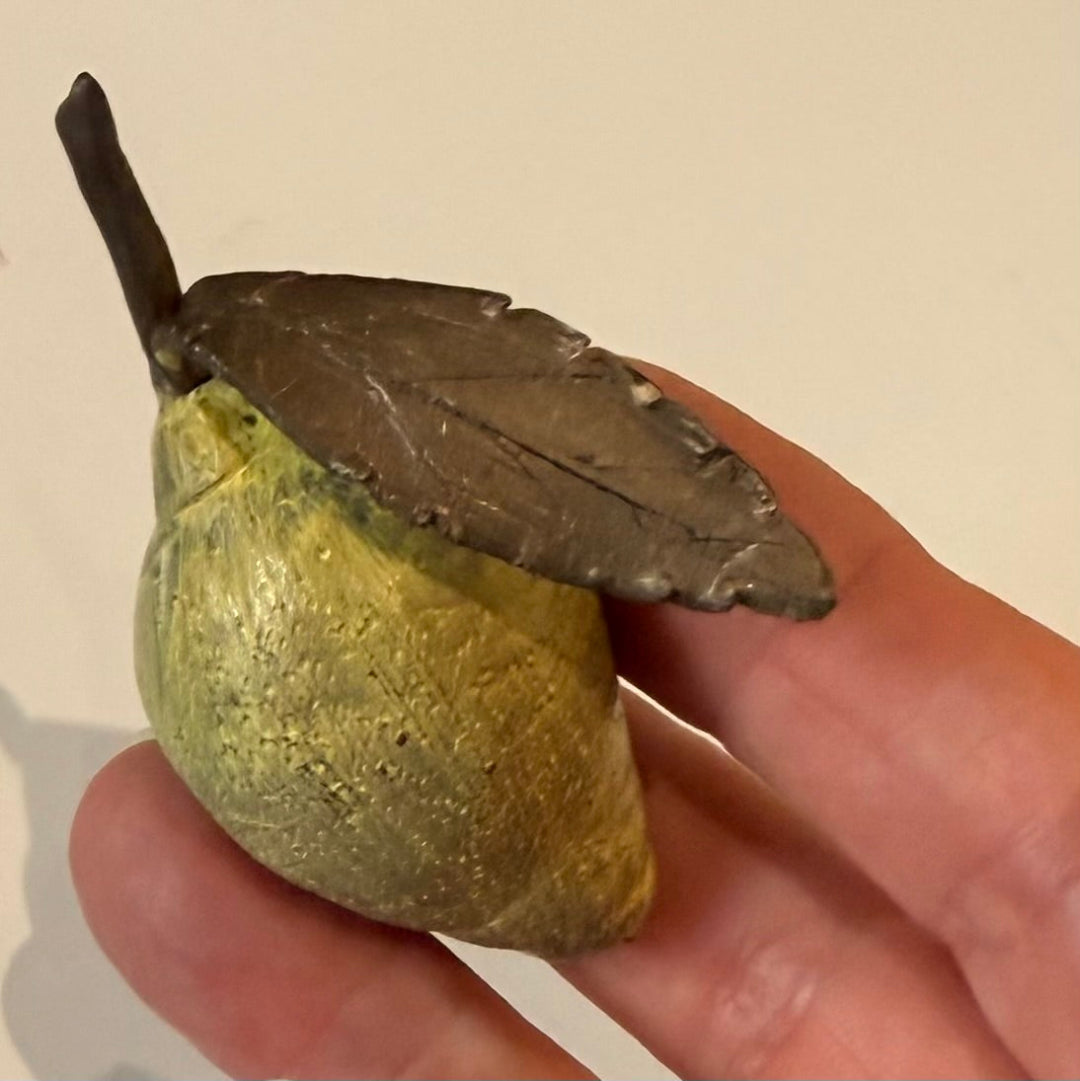 Hand holding a miniature yellow painted cast bronze lemon with a leaf on a beige backgroundbackground