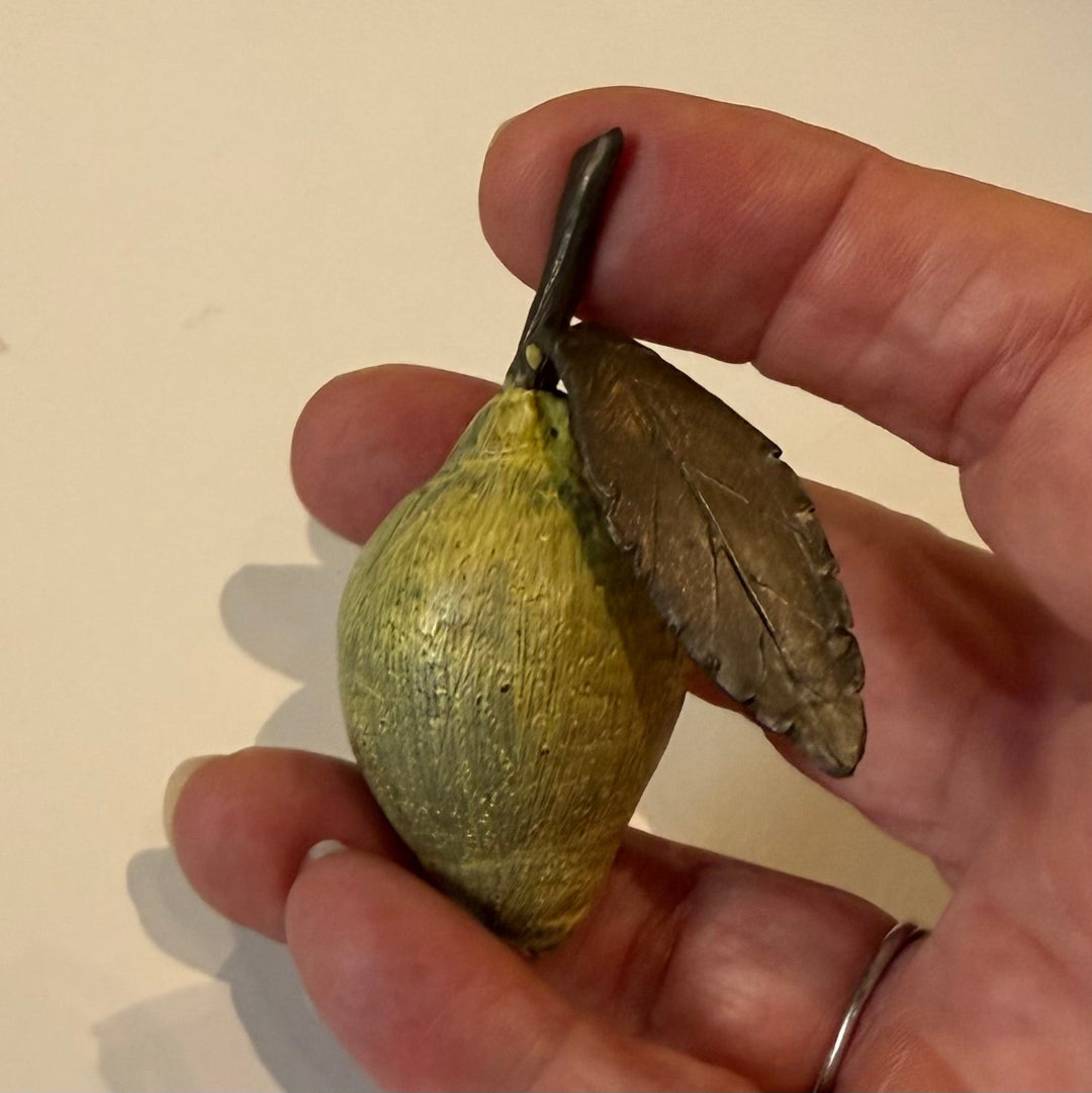 Hand held miniature yellow painted cast bronze lemon with a leaf on a beige background