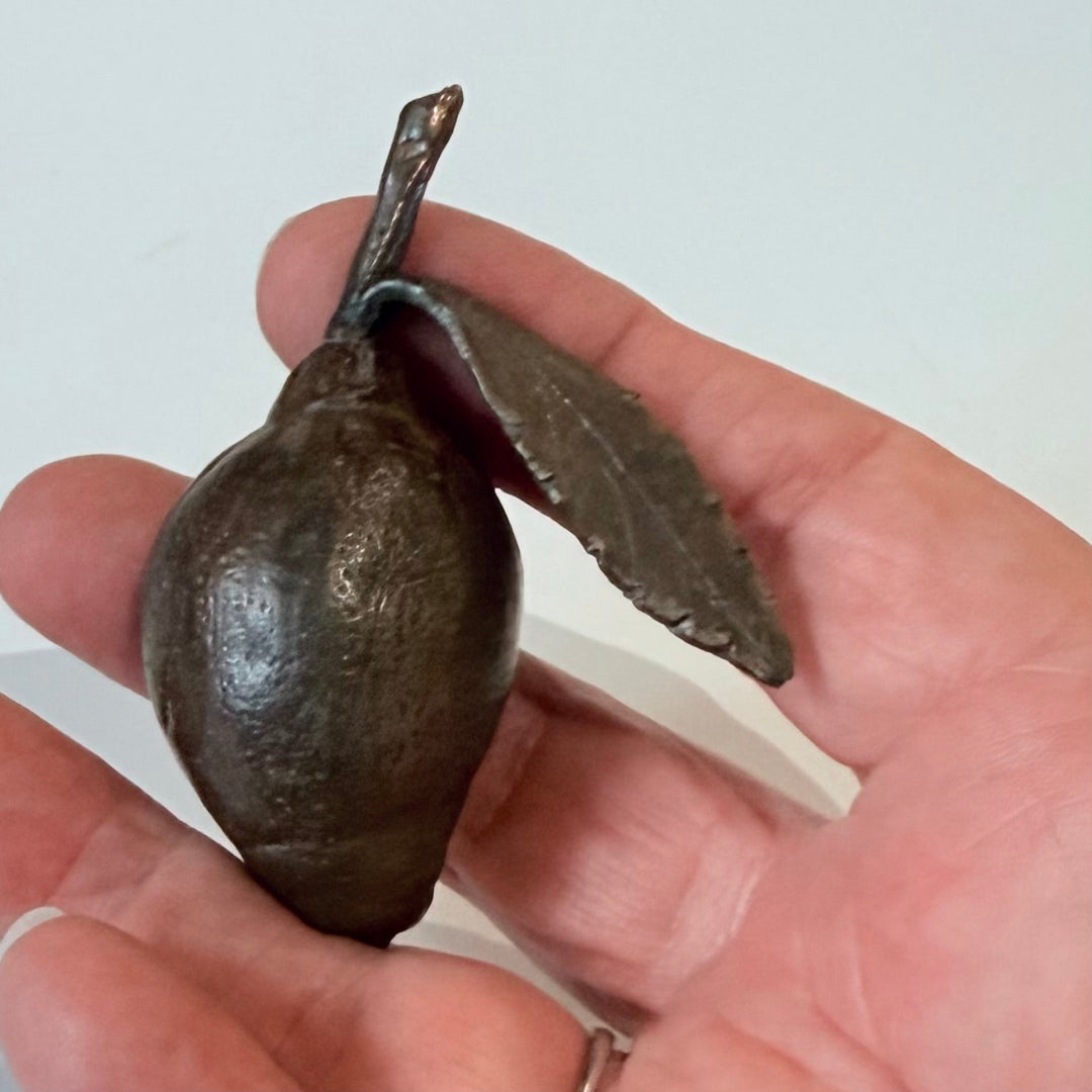 Miniature cast bronze lemon with leaf held in a hand on a plain background