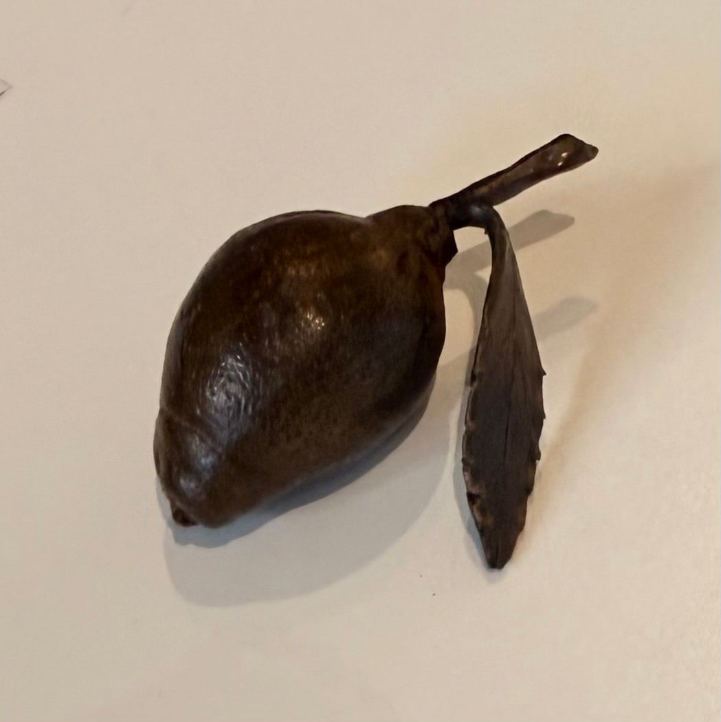 Miniature cast bronze lemon with leaf on a plain background