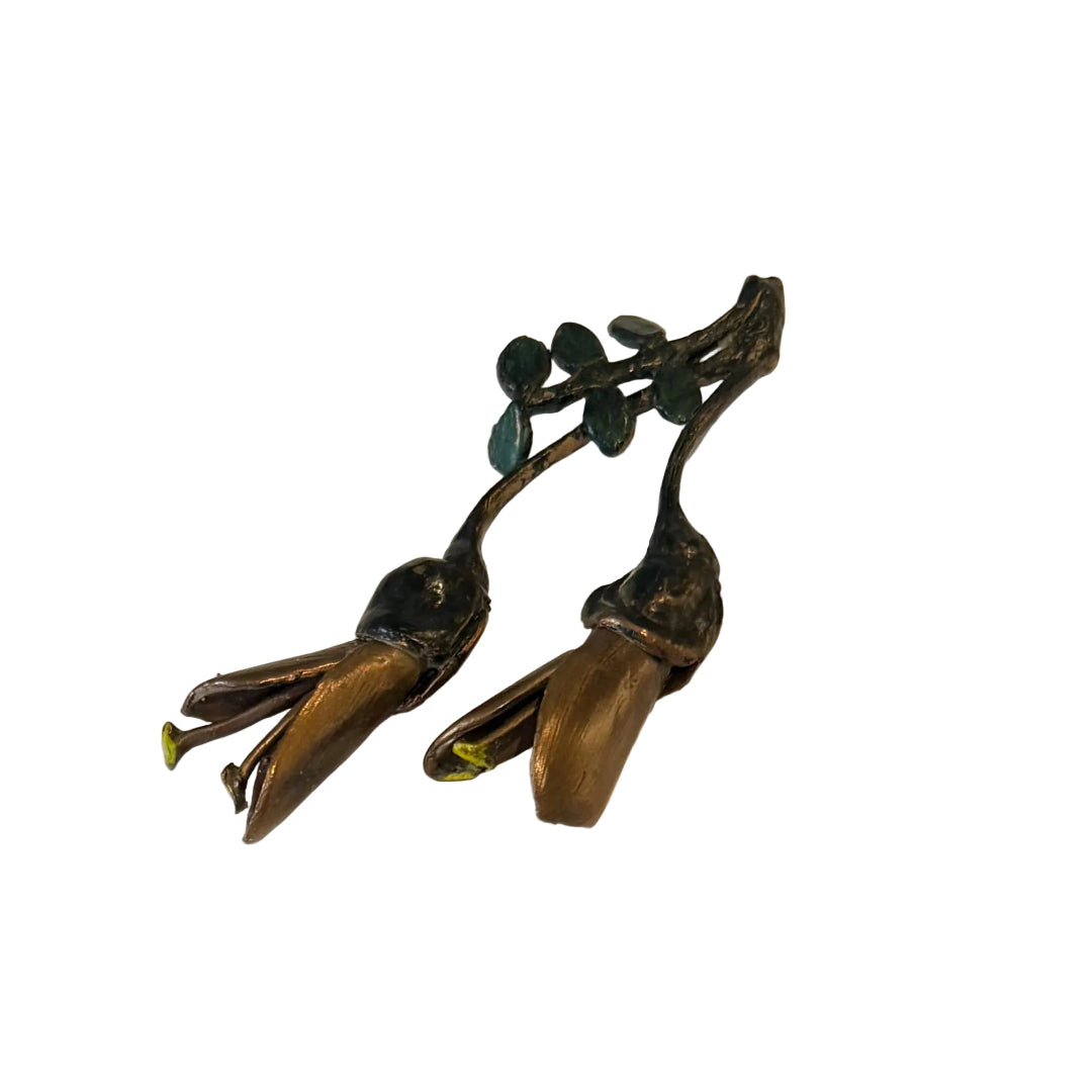 A pair of miniature painted bronze Kowhai flowers with visible seed pods, placed on a plain background.