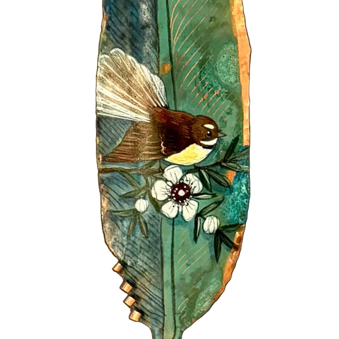 Close up view  of a painted  copper feather with a fantail bird and flower  on a white background