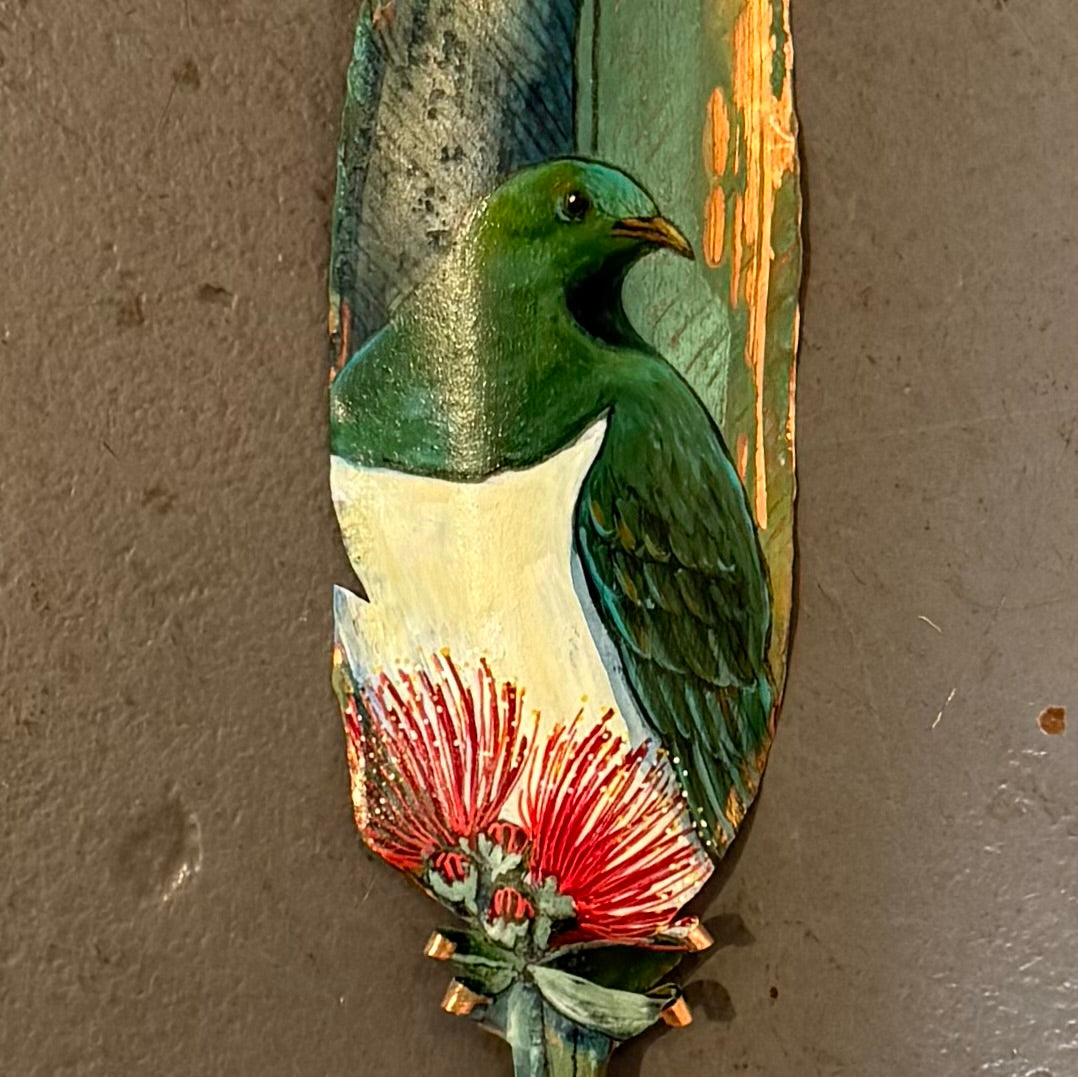 Close up of a painted  copper feather with a Kereru or wood pigeon  and pohutakawa flower  on a white background