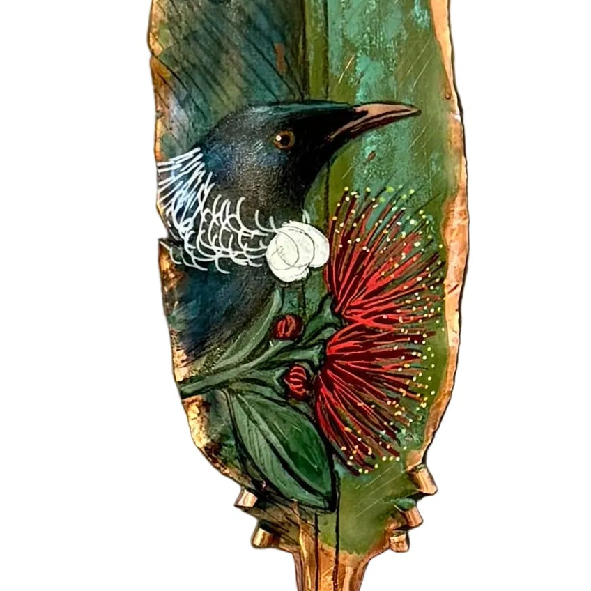 Close up od a decorative copper feather with a painted Tui bird on pohutakawa flower on a white background
