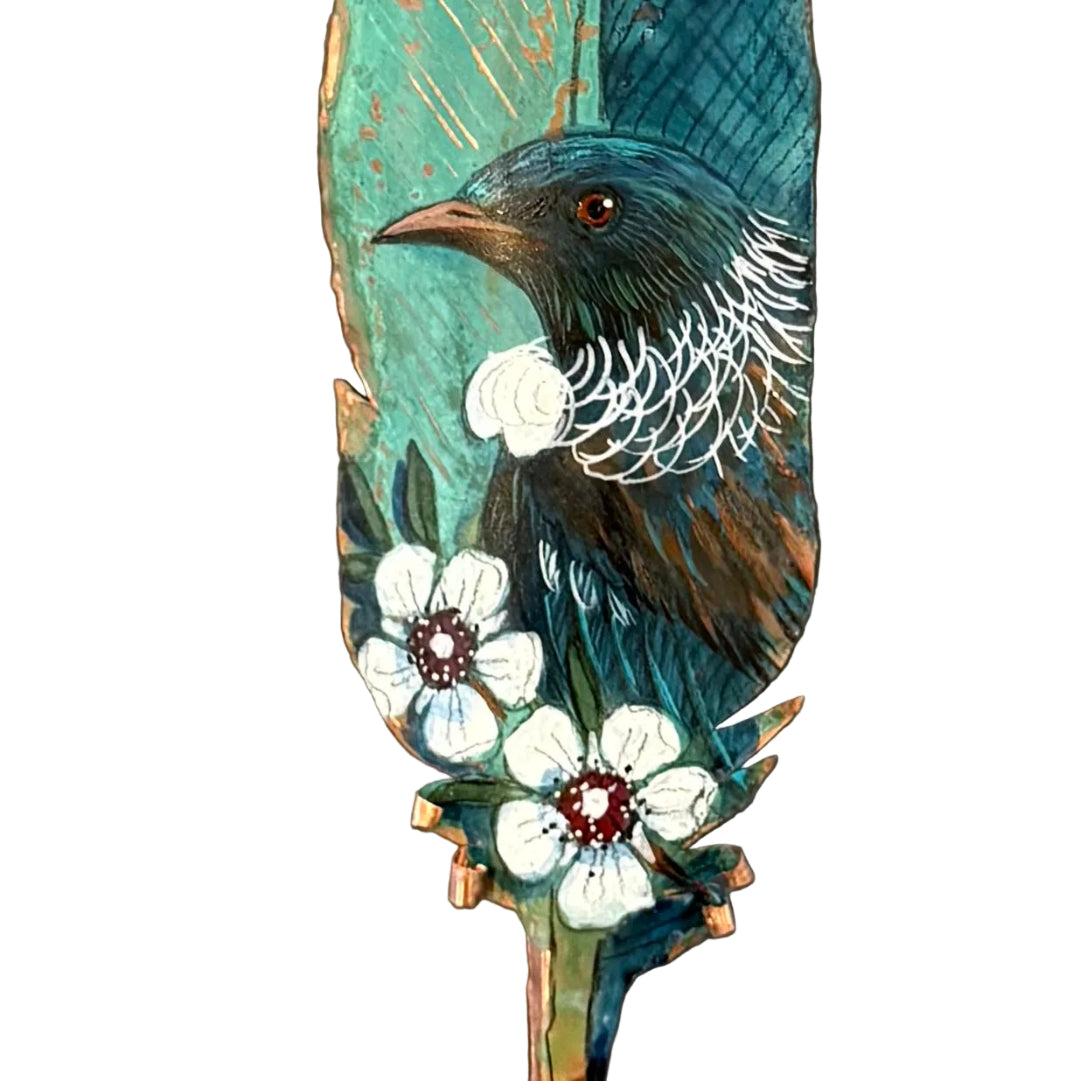 Close up view of  a decorative copper feather with a painted Tui bird and white flowers on a white background
