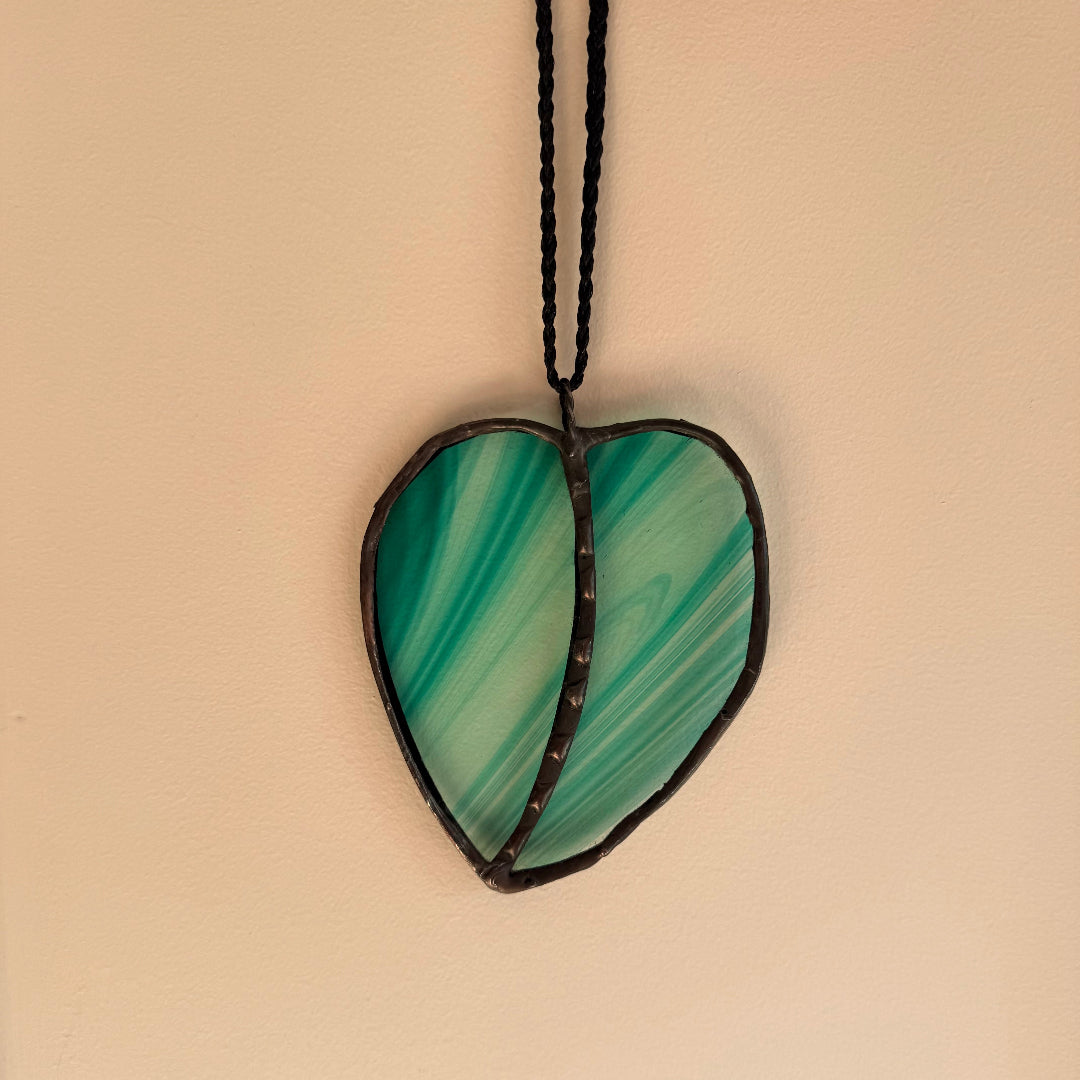 Leaf-shaped green glass wall hanging on a beige background