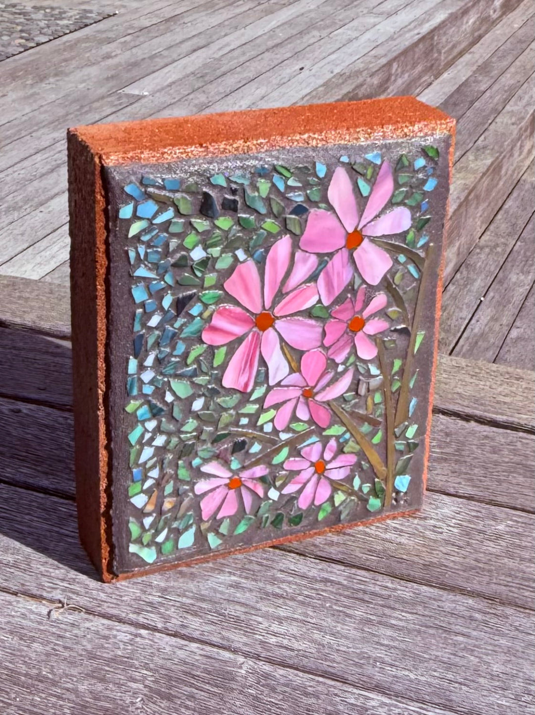 Mosaic artwork on paver of pink flowers on a wooden surface