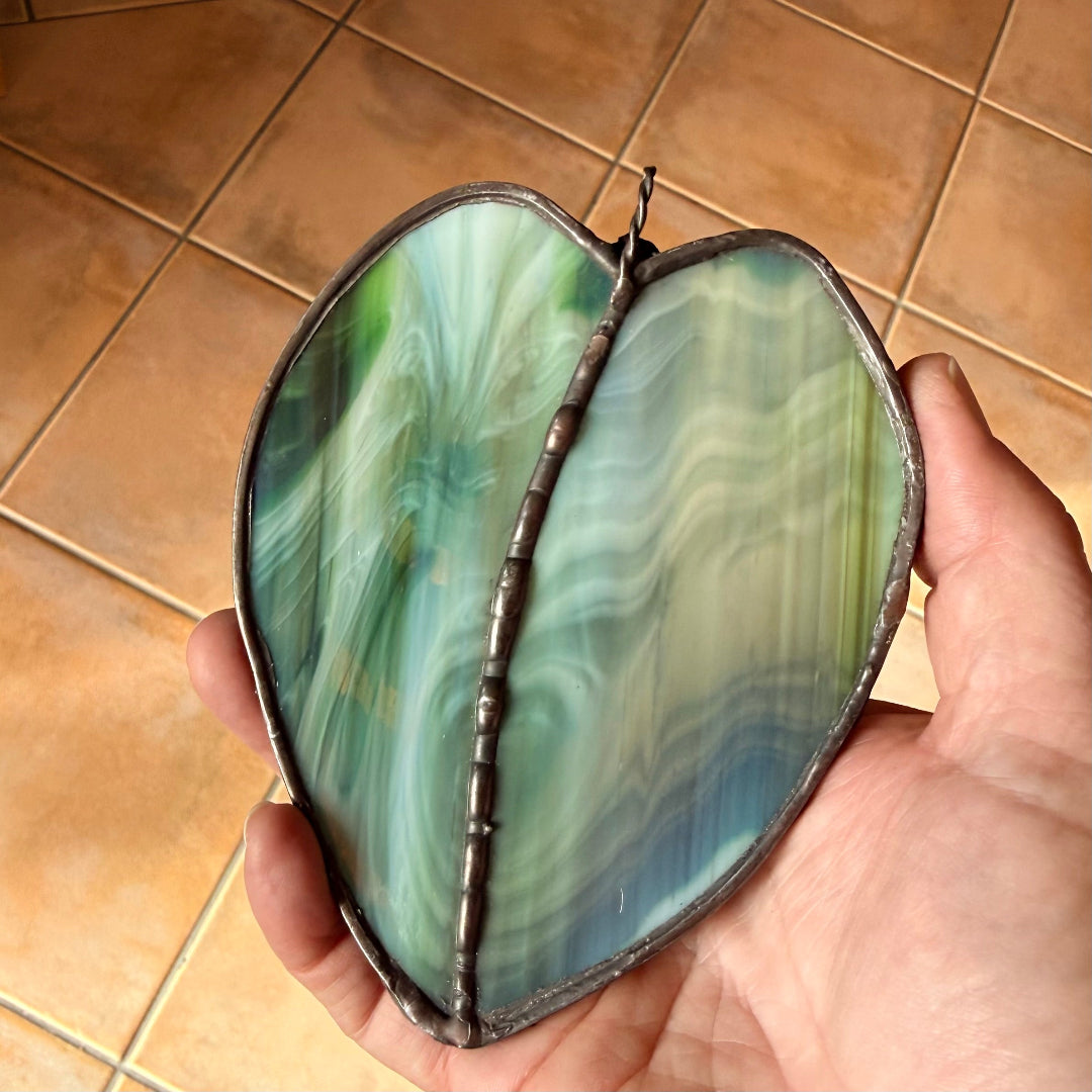 Leaf-shaped stained glass piece held in a hand above a tiled floor