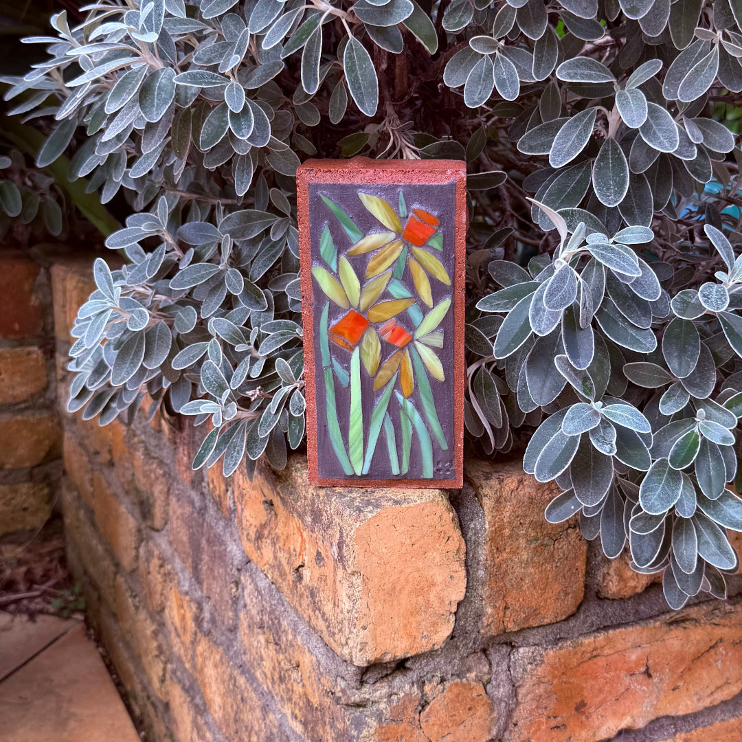 Decorative mosaic brick with floral design on a brick wall surrounded by plants