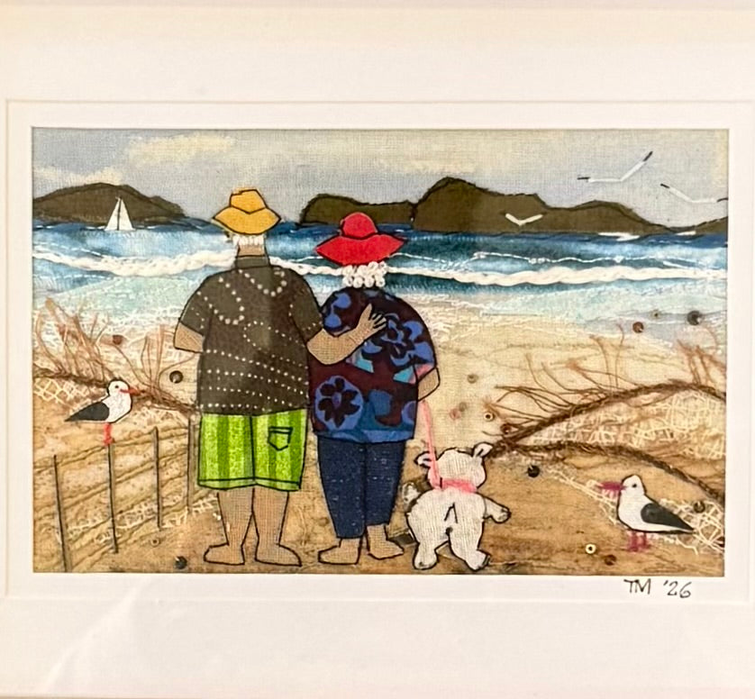Textile artwork of two people and a dog on a beach with birds and mountains in the background.