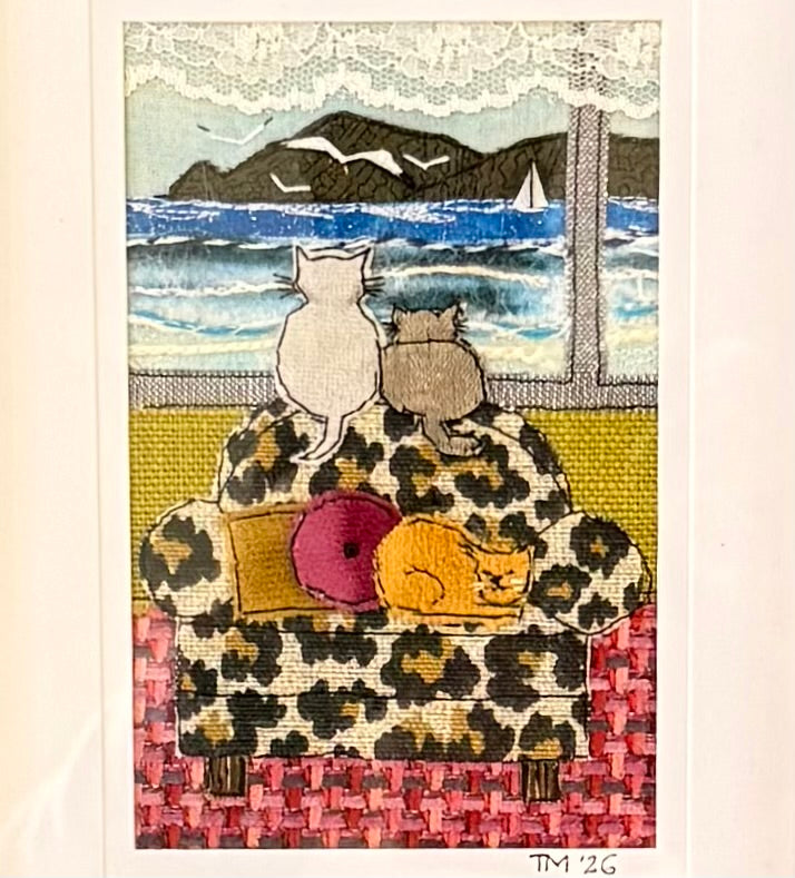 Textile artwork of cats on a leopard print sofa by a seaside.
